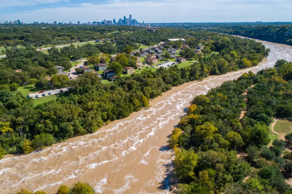 The Colorado River is flooded with brown water with the skyline of Austin, Texas in the background.